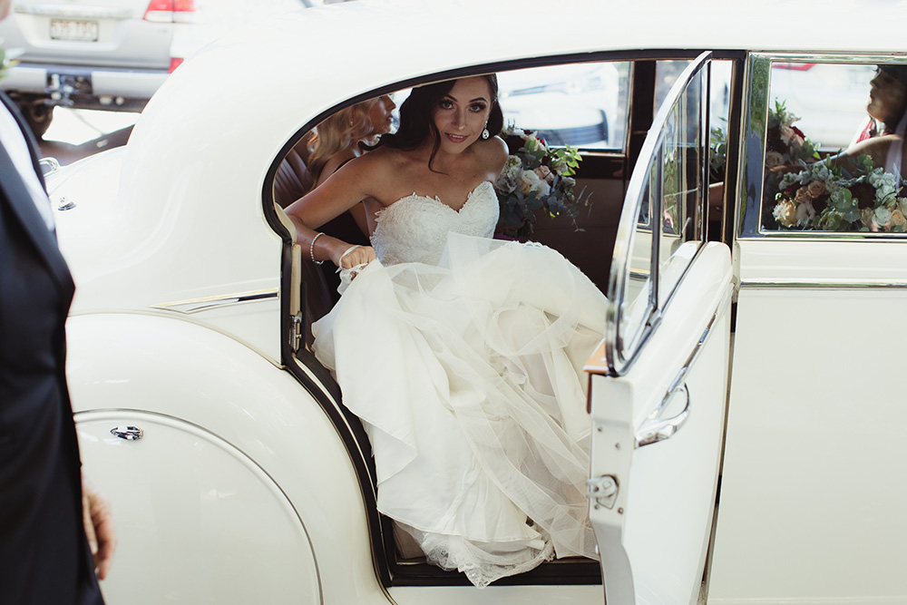 A bride arrives at her ceremony in a white painted wedding car
