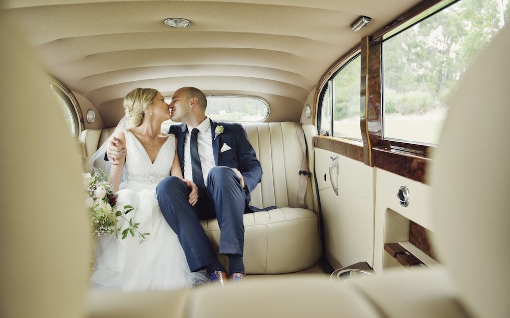 A couple kissing in a jaguar limousines on their wedding day
