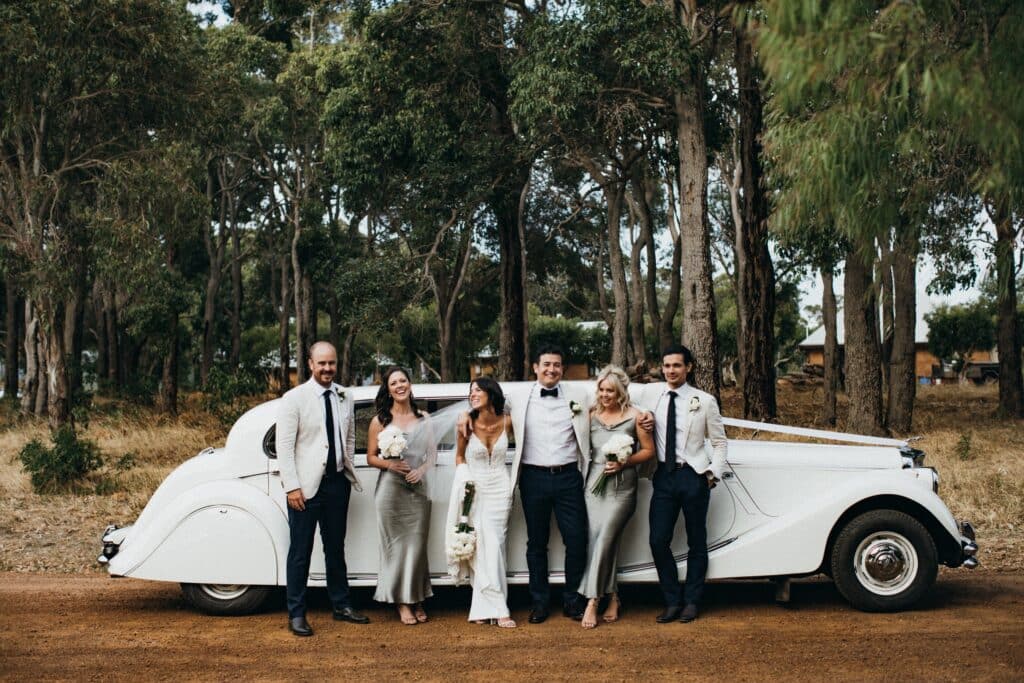 The bridal party and best man's party standing in front of a 1951 MK V Jaguar 7 passenger limousine and smiling in Bunbury